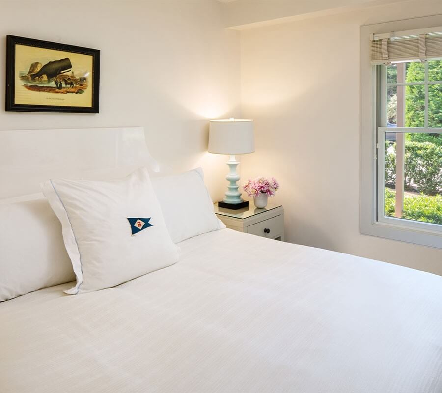 bed with white sheets, nightstand, window overlooking trees